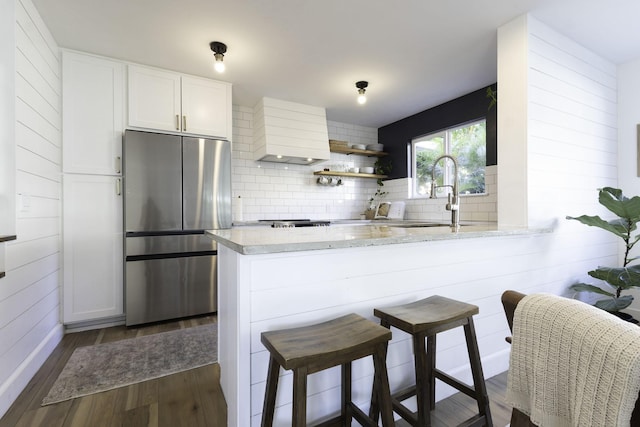 kitchen with stainless steel refrigerator, tasteful backsplash, dark wood-type flooring, a sink, and white cabinets