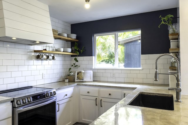 kitchen with stainless steel range with electric stovetop, tasteful backsplash, a sink, light stone counters, and wall chimney range hood