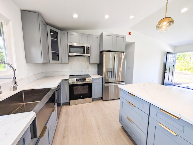 kitchen featuring appliances with stainless steel finishes, gray cabinets, light wood-type flooring, vaulted ceiling, and a sink