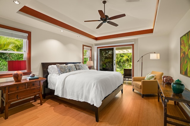 bedroom featuring a tray ceiling, access to exterior, recessed lighting, light wood-style floors, and ceiling fan