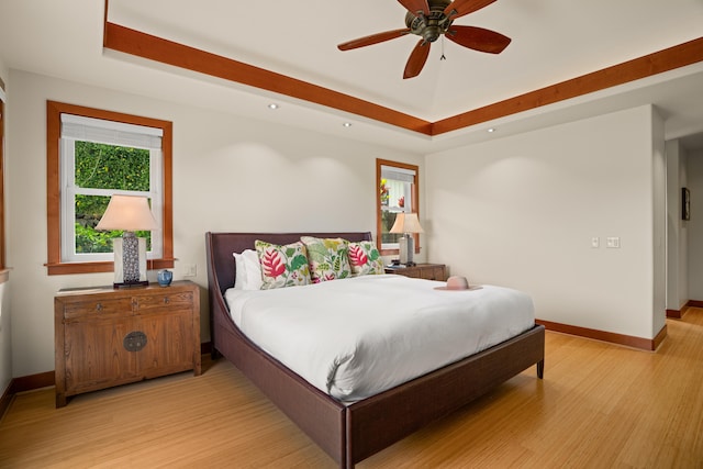 bedroom with light wood-type flooring, a tray ceiling, baseboards, recessed lighting, and a ceiling fan