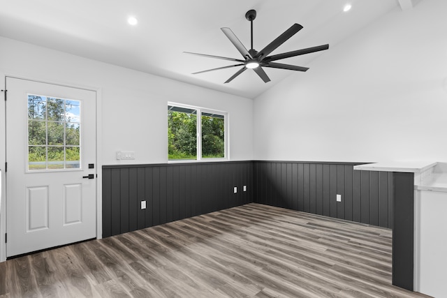 empty room featuring a wainscoted wall, healthy amount of natural light, lofted ceiling, wood finished floors, and a ceiling fan