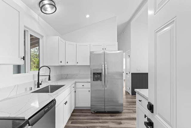 kitchen featuring appliances with stainless steel finishes, a sink, vaulted ceiling, light stone counters, and dark wood-type flooring