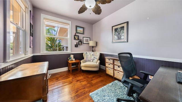 office featuring a healthy amount of sunlight, wood finished floors, a ceiling fan, and a wainscoted wall