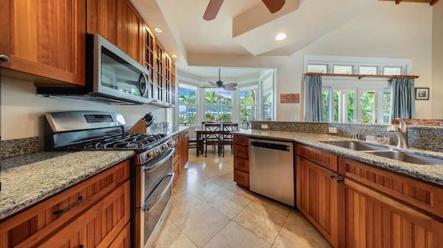 kitchen featuring ceiling fan, light stone countertops, a sink, stainless steel appliances, and brown cabinets