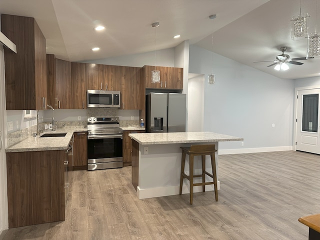 kitchen with appliances with stainless steel finishes, a sink, lofted ceiling, light wood-style floors, and a kitchen bar