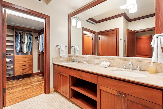 full bath with double vanity, visible vents, a walk in closet, and a sink