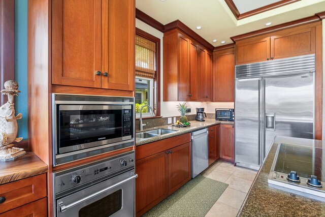 kitchen with dark stone counters, recessed lighting, a sink, built in appliances, and brown cabinetry