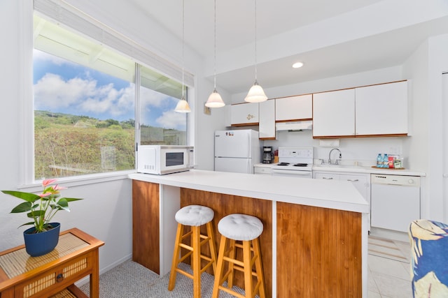 kitchen with white cabinetry, a sink, a breakfast bar, light countertops, and white appliances