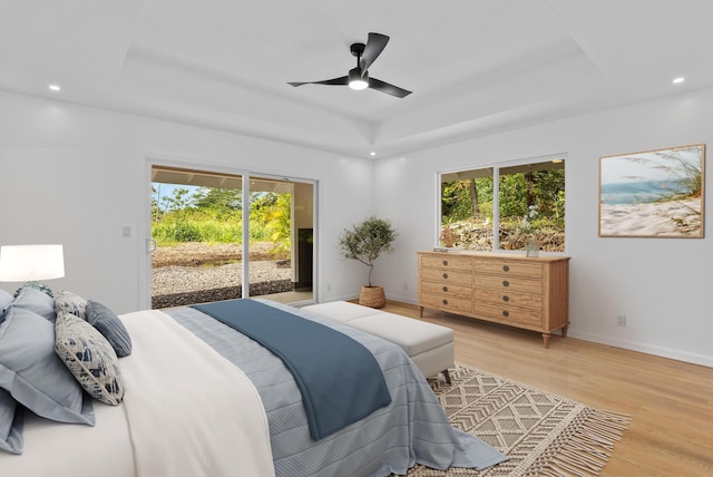 bedroom featuring access to exterior, a tray ceiling, multiple windows, light wood finished floors, and recessed lighting