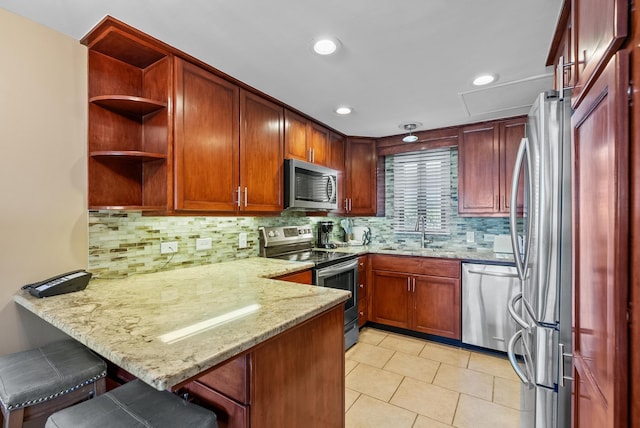 kitchen featuring a peninsula, a sink, tasteful backsplash, light stone counters, and appliances with stainless steel finishes