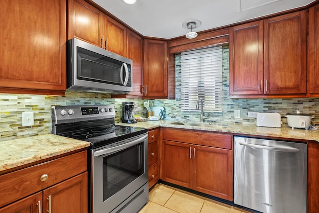 kitchen with appliances with stainless steel finishes, light stone countertops, a sink, and tasteful backsplash