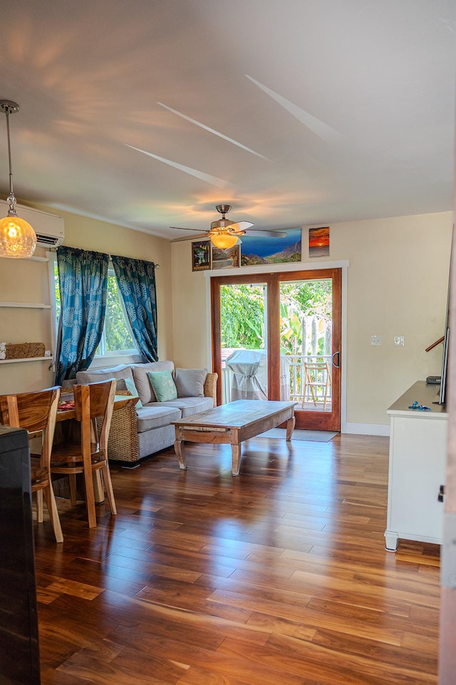 living room with plenty of natural light, a ceiling fan, a wall unit AC, and wood finished floors