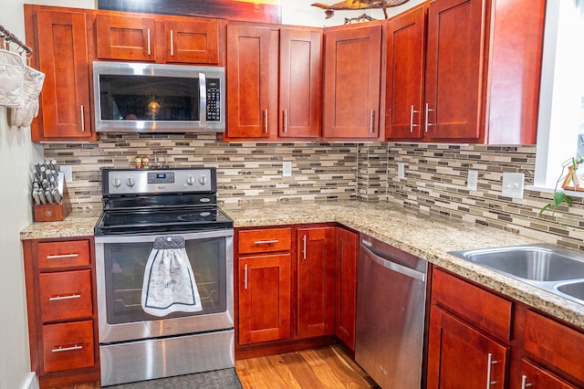kitchen with tasteful backsplash, light stone counters, reddish brown cabinets, light wood-style flooring, and appliances with stainless steel finishes