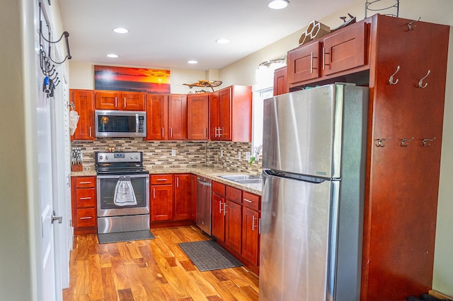 kitchen with recessed lighting, backsplash, light wood-style floors, light stone counters, and appliances with stainless steel finishes