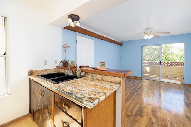 kitchen with a ceiling fan, wood finished floors, a sink, baseboards, and a peninsula
