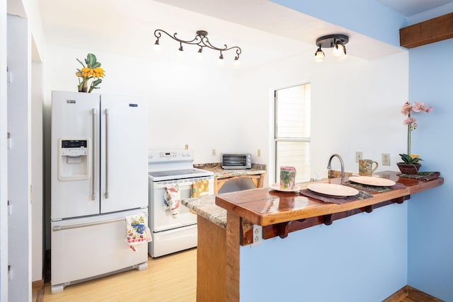 kitchen with a peninsula, a breakfast bar, white appliances, light countertops, and light wood-style flooring