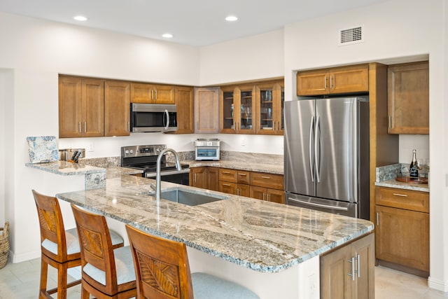 kitchen featuring appliances with stainless steel finishes, a sink, brown cabinetry, a breakfast bar, and recessed lighting