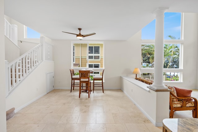 dining area featuring decorative columns, stairway, ceiling fan, baseboards, and light tile patterned floors