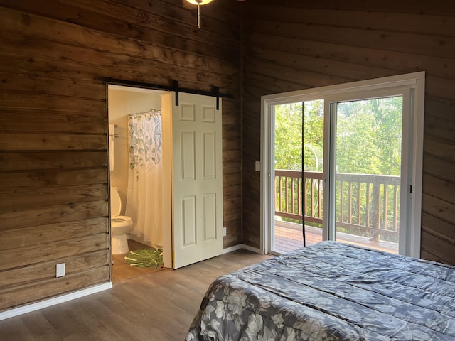bedroom with wooden walls, wood finished floors, connected bathroom, and access to exterior