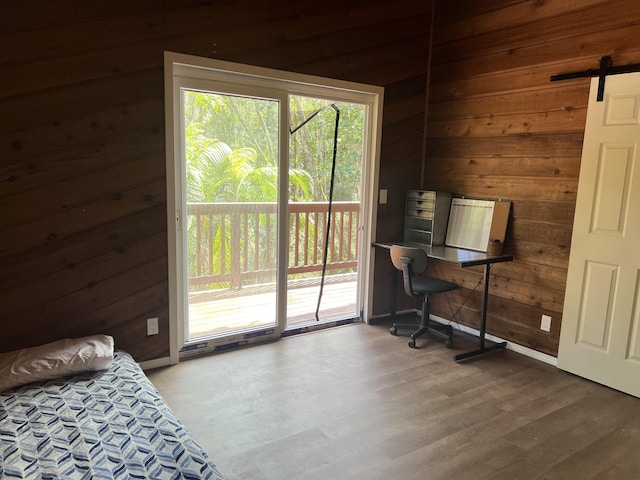 bedroom with wooden walls, wood finished floors, access to outside, and a barn door