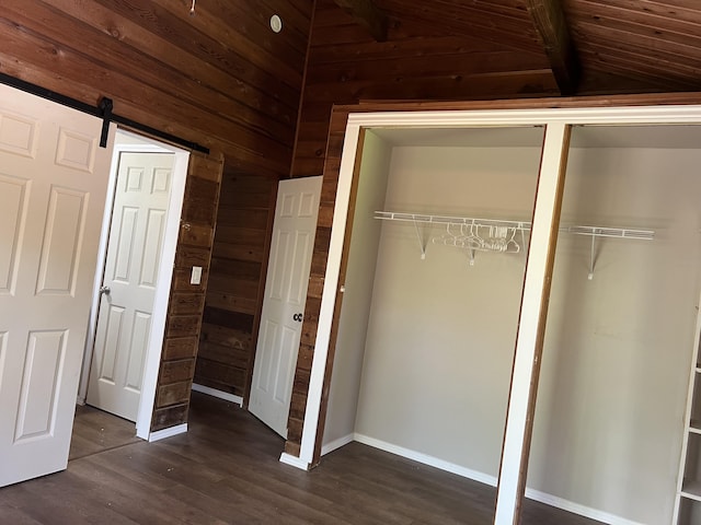 unfurnished bedroom featuring a barn door, wood walls, baseboards, lofted ceiling, and dark wood-style floors