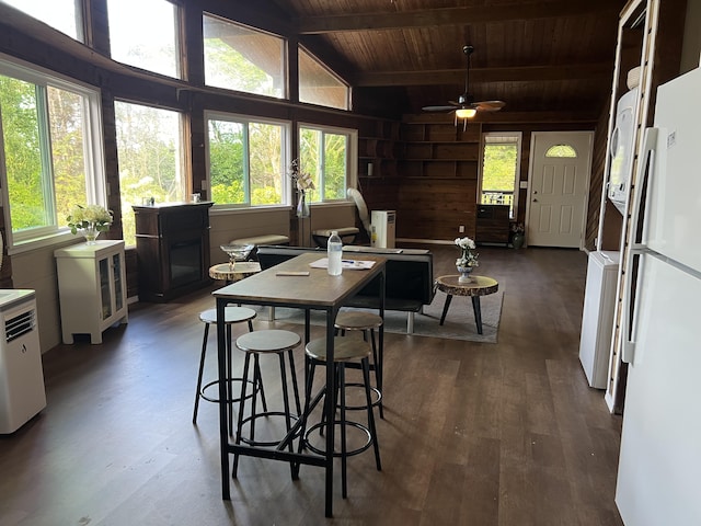 dining room featuring a ceiling fan, vaulted ceiling with beams, wood ceiling, wood walls, and dark wood-style flooring