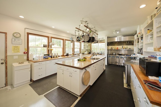 kitchen featuring open shelves, black microwave, a sink, wood counters, and white cabinetry