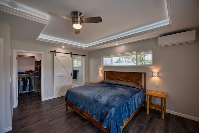 bedroom featuring wood finished floors, a barn door, a spacious closet, a wall unit AC, and a tray ceiling