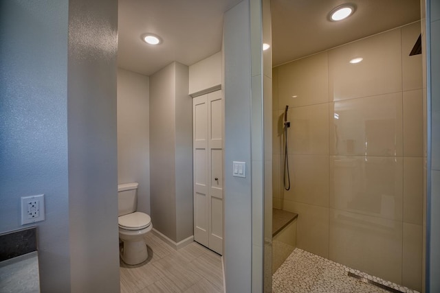 full bath featuring toilet, tiled shower, and baseboards
