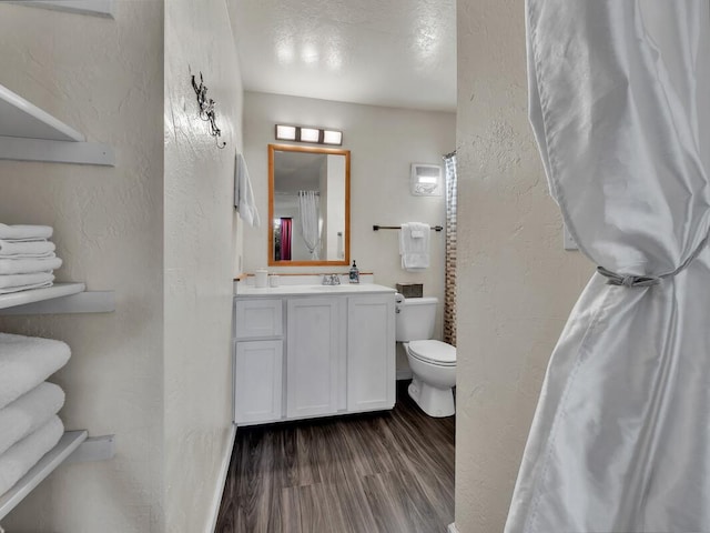 bathroom with toilet, vanity, a textured wall, and wood finished floors