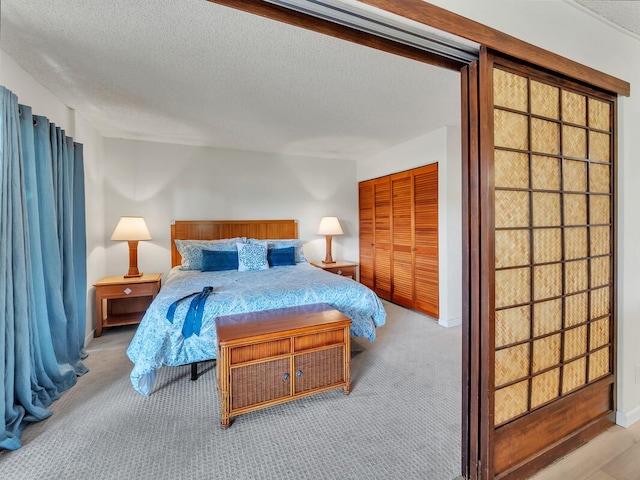 bedroom featuring baseboards, a textured ceiling, a closet, and light colored carpet