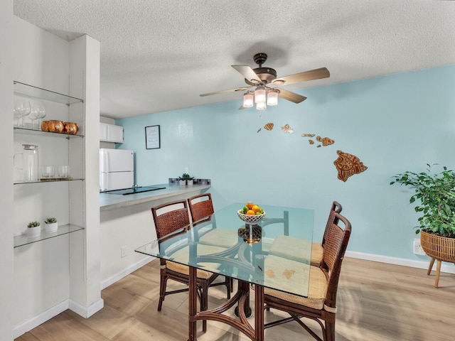 dining space featuring baseboards, ceiling fan, a textured ceiling, and light wood finished floors
