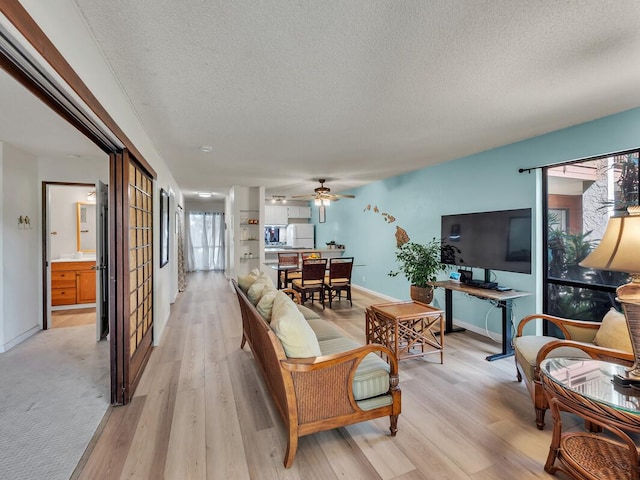 living area with light wood-style floors, baseboards, ceiling fan, and a textured ceiling