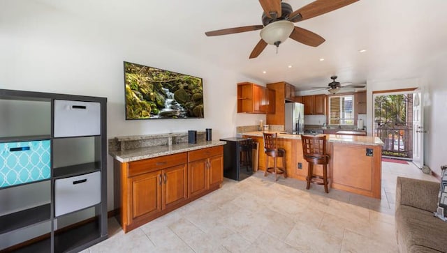 kitchen with freestanding refrigerator, a ceiling fan, brown cabinetry, and a peninsula