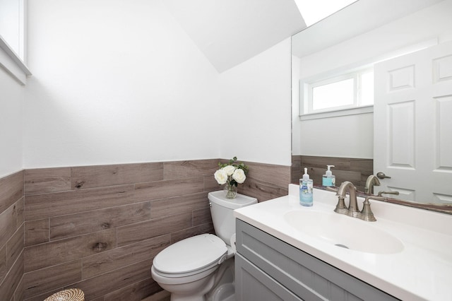 bathroom featuring vanity, toilet, tile walls, and a wainscoted wall