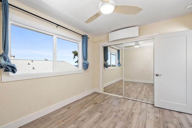 unfurnished bedroom with a closet, baseboards, light wood-type flooring, a wall mounted AC, and a ceiling fan