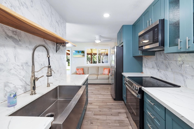 kitchen with blue cabinetry, appliances with stainless steel finishes, open shelves, a sink, and light wood finished floors
