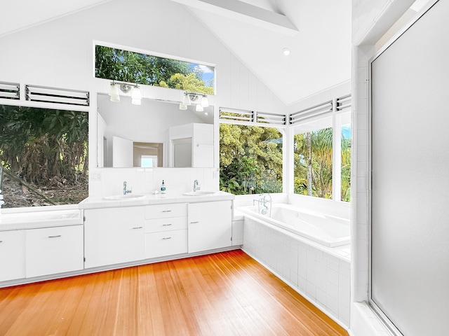 full bathroom with lofted ceiling, plenty of natural light, a bath, wood finished floors, and double vanity