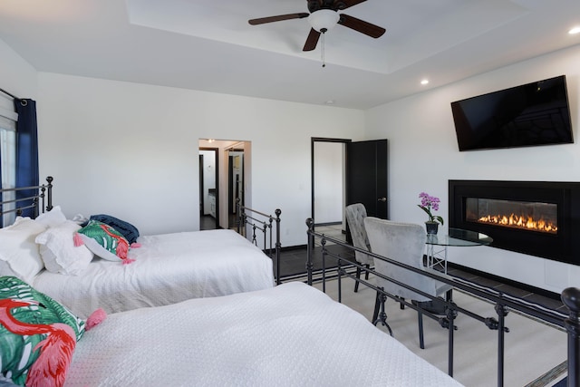 bedroom with recessed lighting, ceiling fan, a raised ceiling, and a glass covered fireplace
