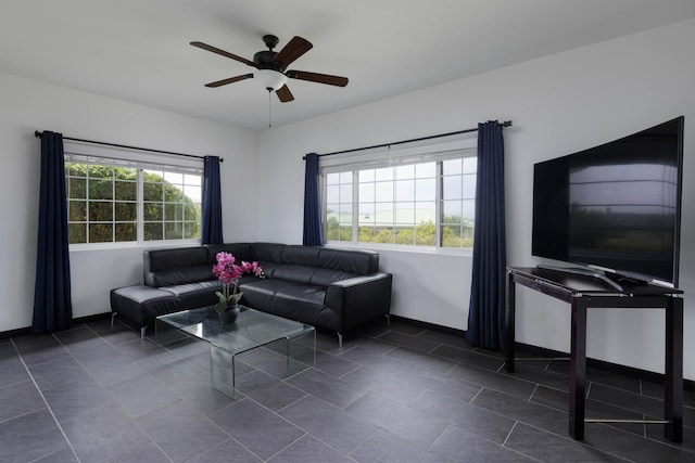 living area featuring a ceiling fan, dark tile patterned floors, and baseboards