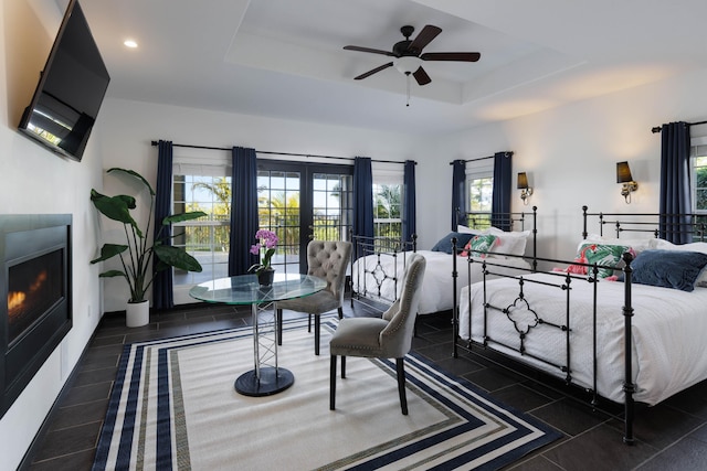 bedroom featuring tile patterned flooring, recessed lighting, a tray ceiling, and a warm lit fireplace