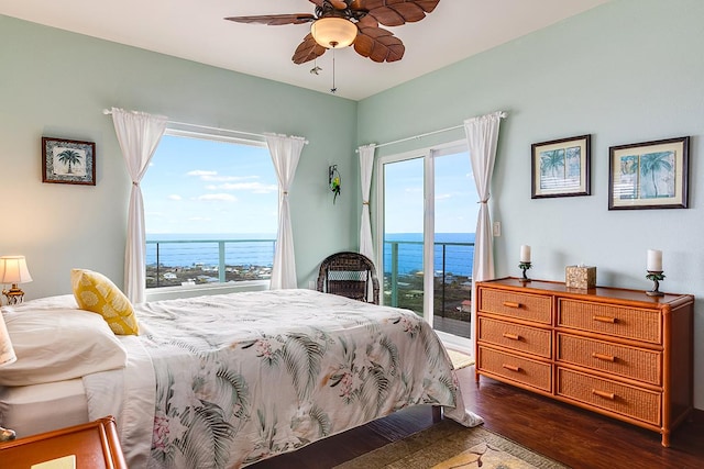 bedroom with dark wood finished floors, a water view, multiple windows, and access to exterior