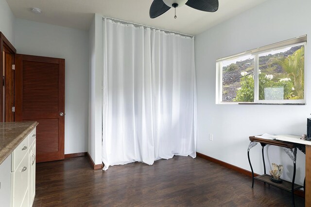 unfurnished dining area featuring baseboards, a ceiling fan, and dark wood-style flooring