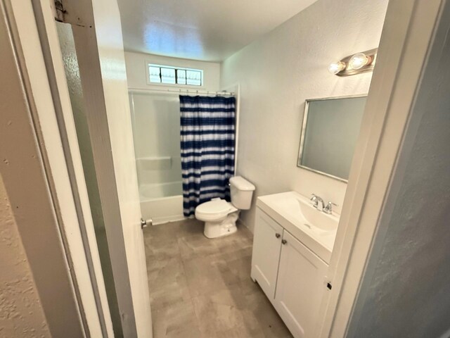 bathroom featuring shower / tub combo with curtain, vanity, toilet, and a textured wall