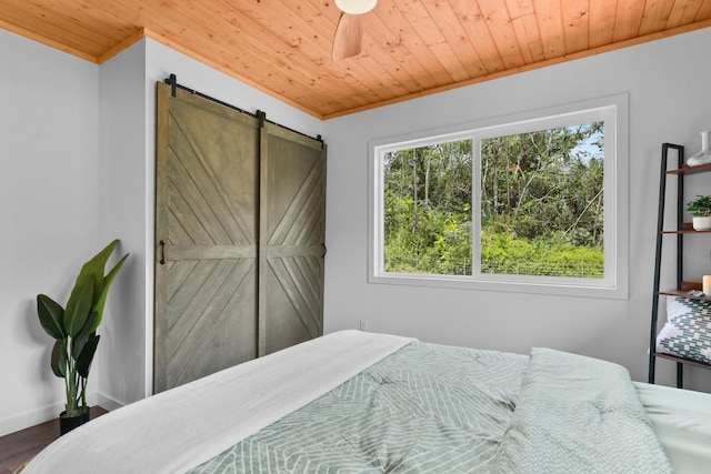 bedroom with wood ceiling, a barn door, wood finished floors, and ornamental molding