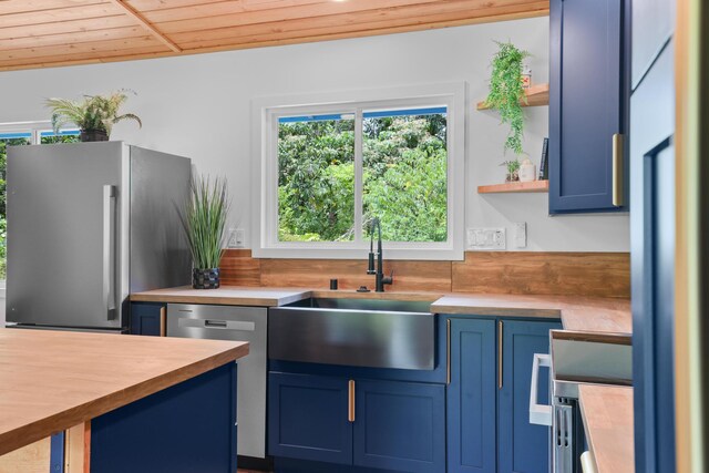 kitchen with wood counters, appliances with stainless steel finishes, blue cabinets, a sink, and wooden ceiling