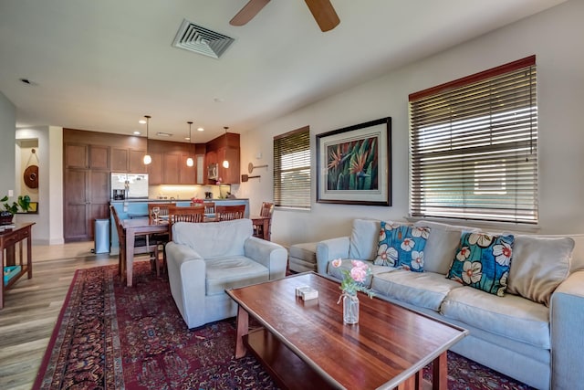 living room featuring visible vents, a ceiling fan, light wood-style floors, and a healthy amount of sunlight