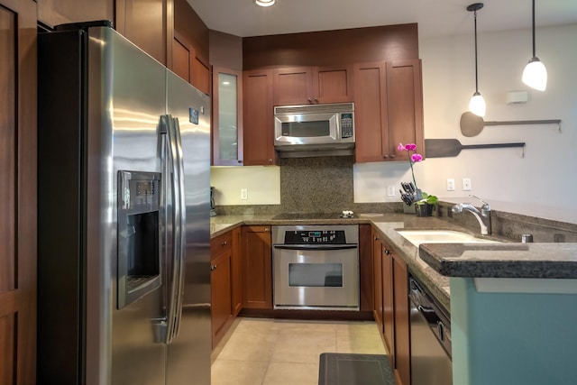 kitchen featuring brown cabinetry, glass insert cabinets, appliances with stainless steel finishes, light tile patterned floors, and decorative light fixtures