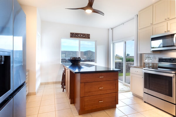 kitchen featuring a ceiling fan, dark countertops, a center island, light tile patterned floors, and stainless steel appliances